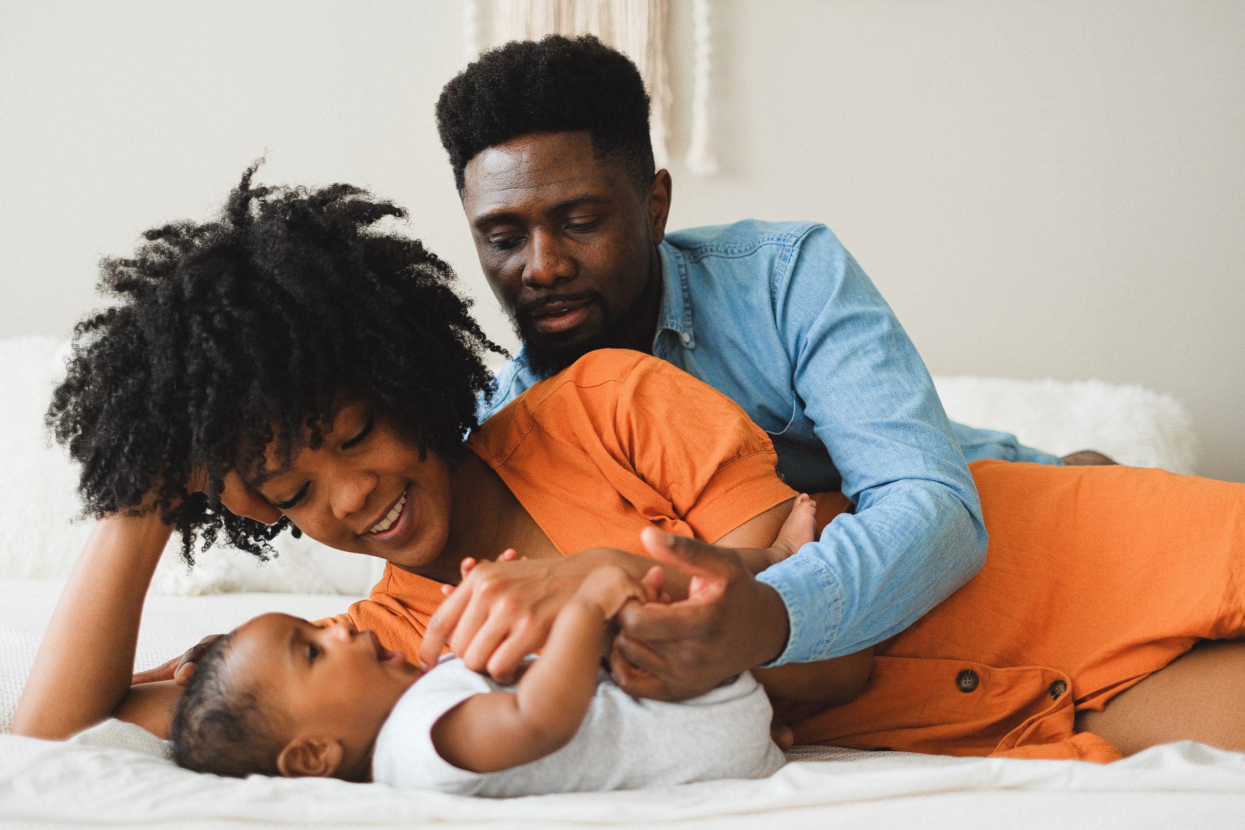 Eine fröhliche afroamerikanische Familie mit einem Baby auf dem Bett, die liebevolle Momente teilt, ein Bild, das die Bedeutung der finanziellen Absicherung durch eine Restkreditversicherung für unvorhergesehene Ereignisse im Familienleben symbolisiert.