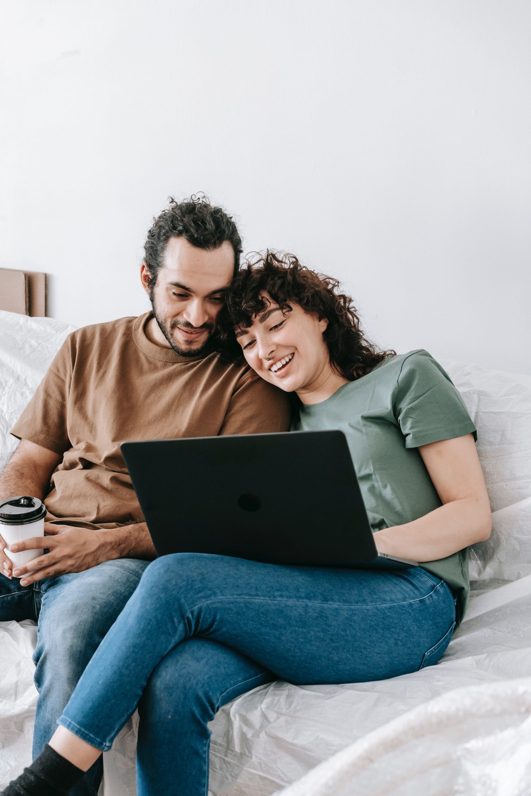 Glückliches Paar, das gemeinsam auf einem Bett sitzt und auf einem Laptop recherchiert, vielleicht um günstige Kredite zu vergleichen oder einen Online-Kreditantrag zu stellen, in einem gemütlichen häuslichen Umfeld.