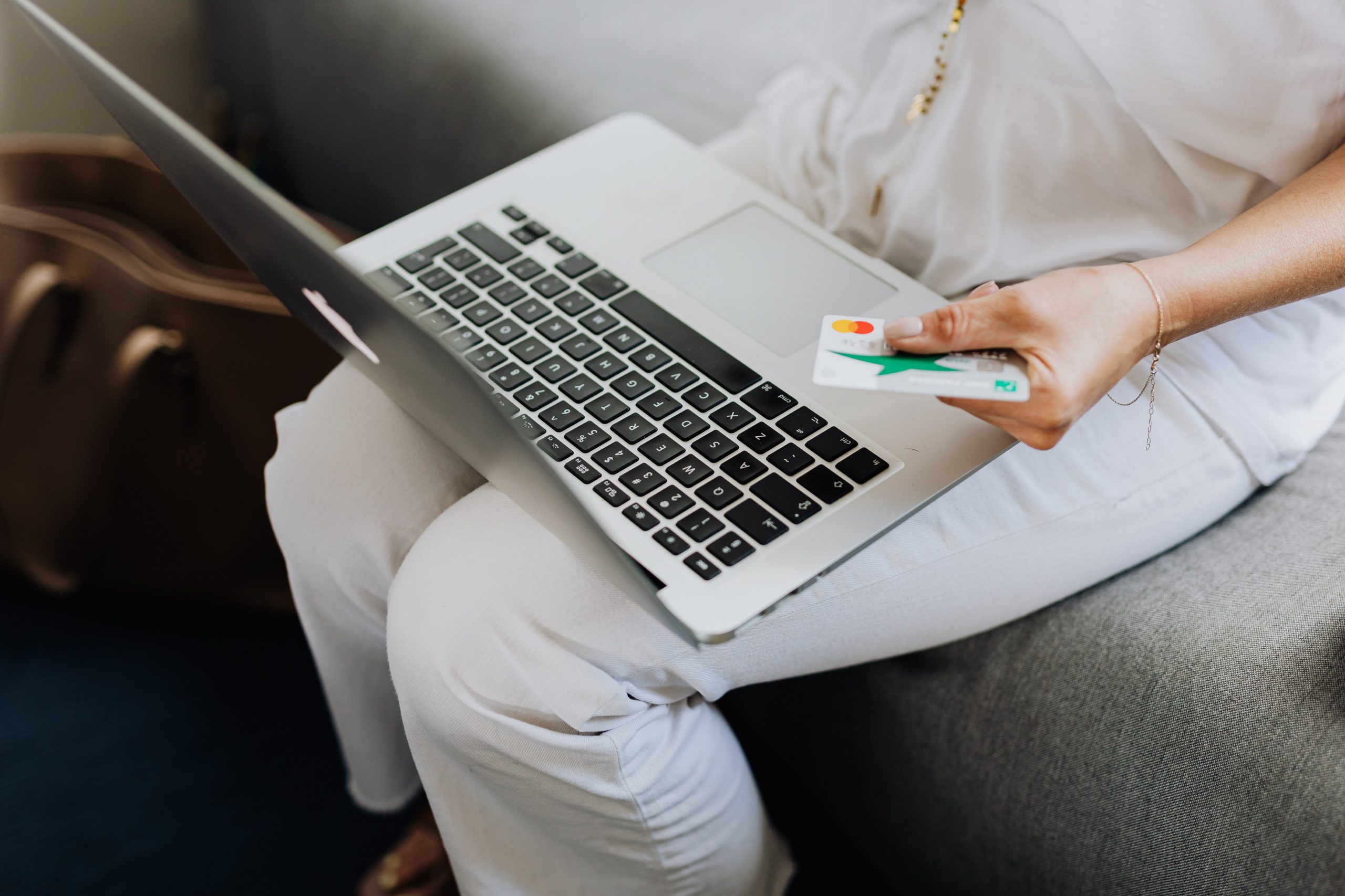 Eine Person in weißer Kleidung sitzt mit einem Laptop auf dem Schoß und hält eine Bankkarte, was die moderne, digitale Finanzberatung und das Online-Banking von zu Hause aus darstellt.