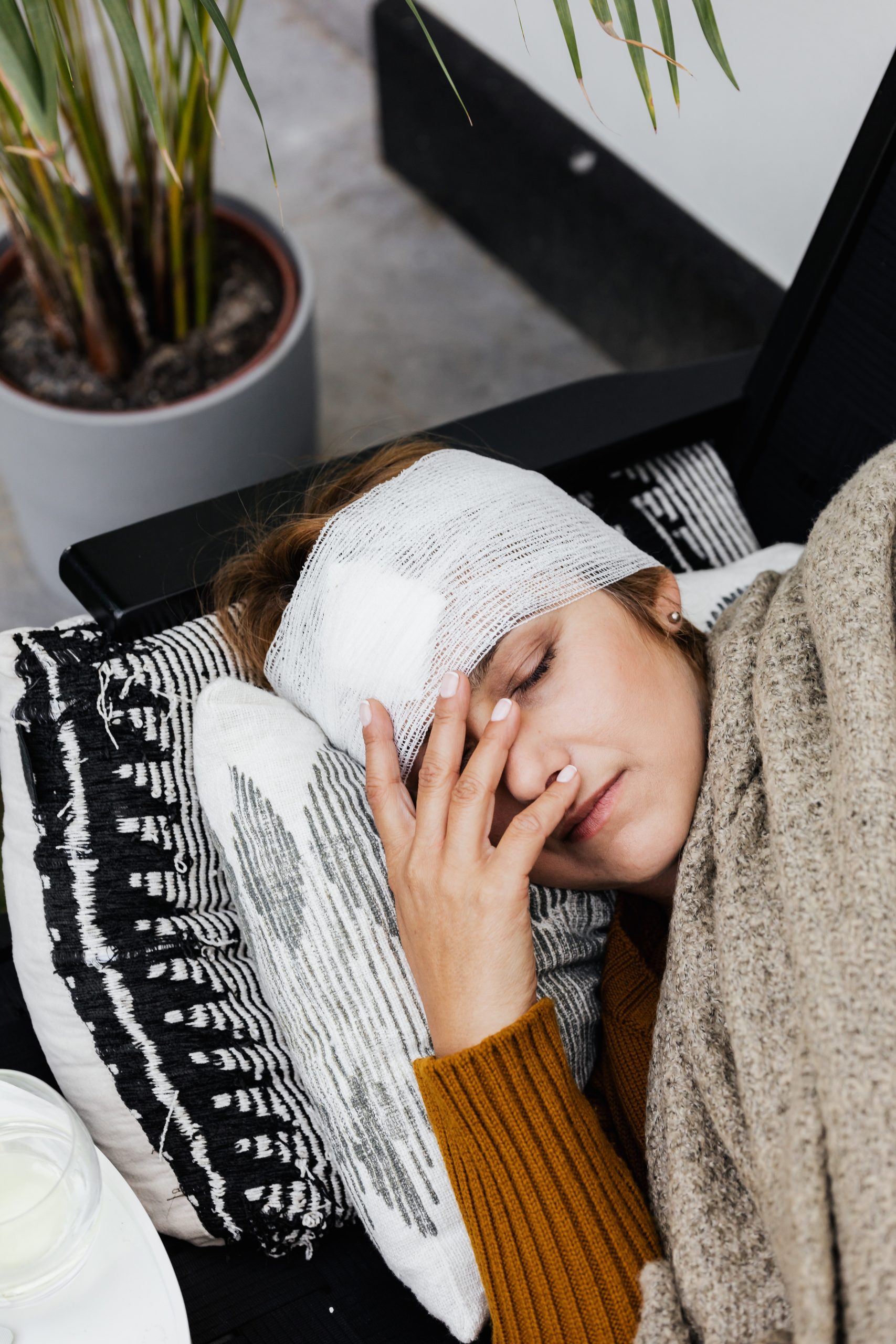 Eine Frau mit einem Kopfverband liegt erschöpft auf einem Sofa, eine Szene, die die Bedeutung einer Unfallversicherung für individuellen Schutz und finanzielle Unterstützung im Falle von häuslichen Unfällen hervorhebt.