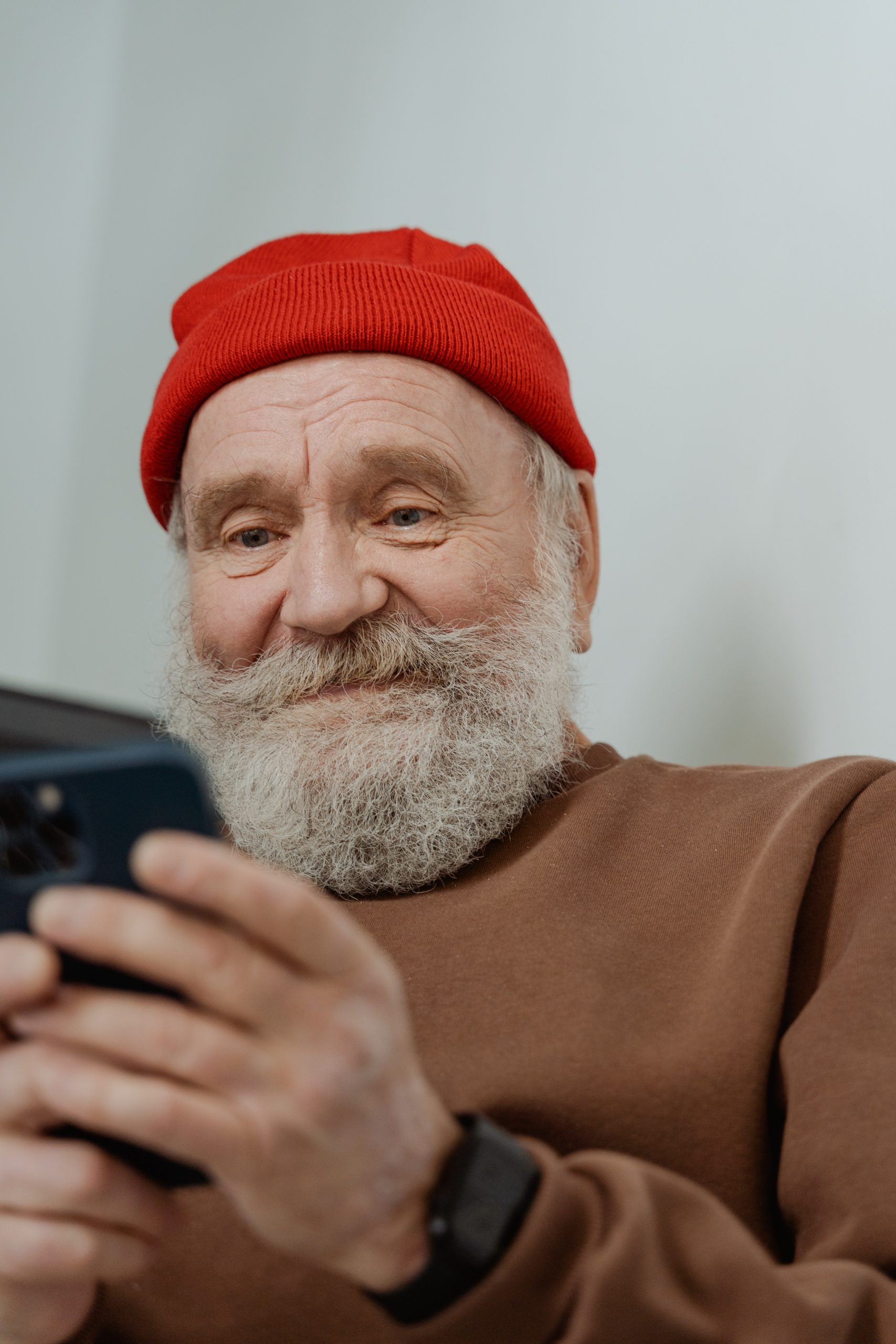 Ein älterer Mann mit einem roten Hut und einem freundlichen Lächeln benutzt ein Smartphone, was zeigt, dass die moderne Altersvorsorge auch digitale Kompetenzen für das Management von Vorsorgekonten und Investitionen im Ruhestand umfasst.