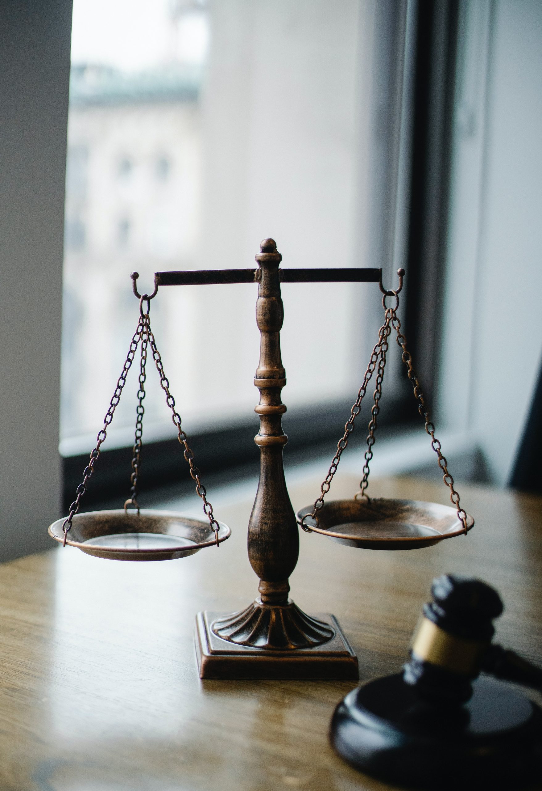 Eine klassische Waage der Justiz auf einem Tisch, neben einem Richterhammer, symbolisch für Recht und Gerechtigkeit, was die Bedeutung einer Rechtsschutzversicherung für den juristischen Beistand in rechtlichen Angelegenheiten darstellt.
