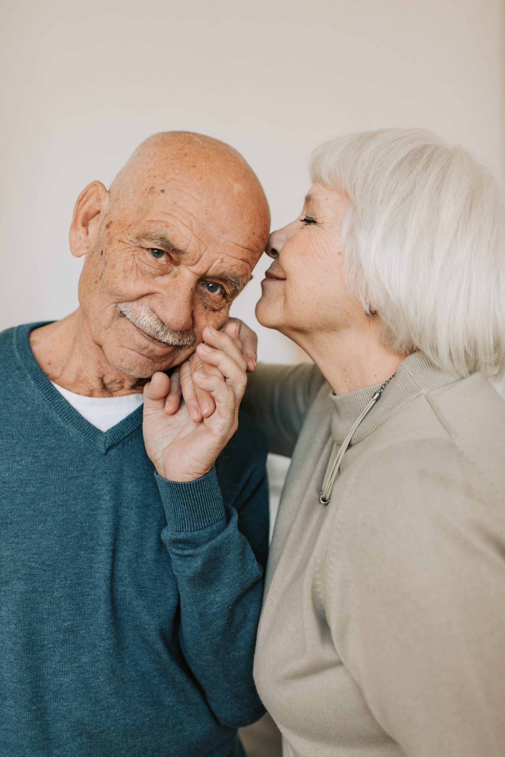 Ein liebevolles älteres Paar, wobei die Frau ihren Partner auf die Wange küsst, ein Bild, das die Wichtigkeit von emotionaler und finanzieller Vorsorge für ein sorgenfreies und glückliches Zusammenleben im Alter symbolisiert.
